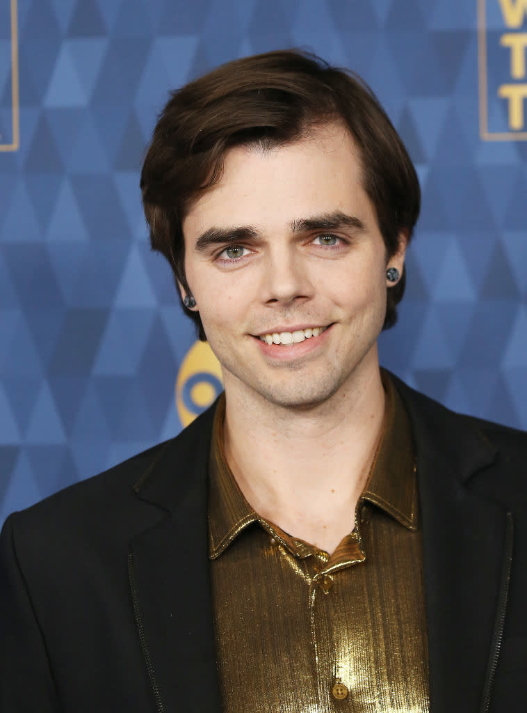 Reid in a black jacket over a gold shirt posing for the camera