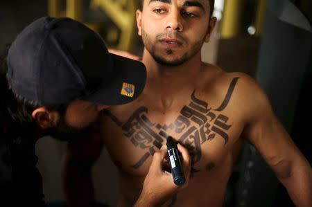 Palestinian artist Bilal Khalid paints Arabic letters on a bodybuilder in a gym in Gaza City April 12, 2016. REUTERS/Mohammed Salem