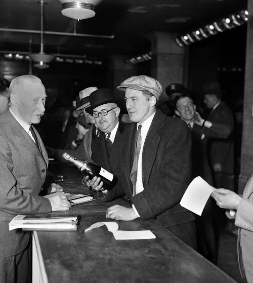 One man holds a bottle of champagne at a busy department store counter.