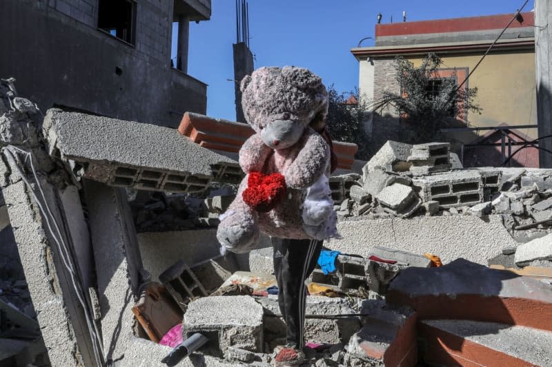 A Palestinian boy carries a stuffed toy while walking on the rubble of a house belonging to the Al-Faqawi family following an Israeli airstrike. Abed Rahim Khatib/dpa