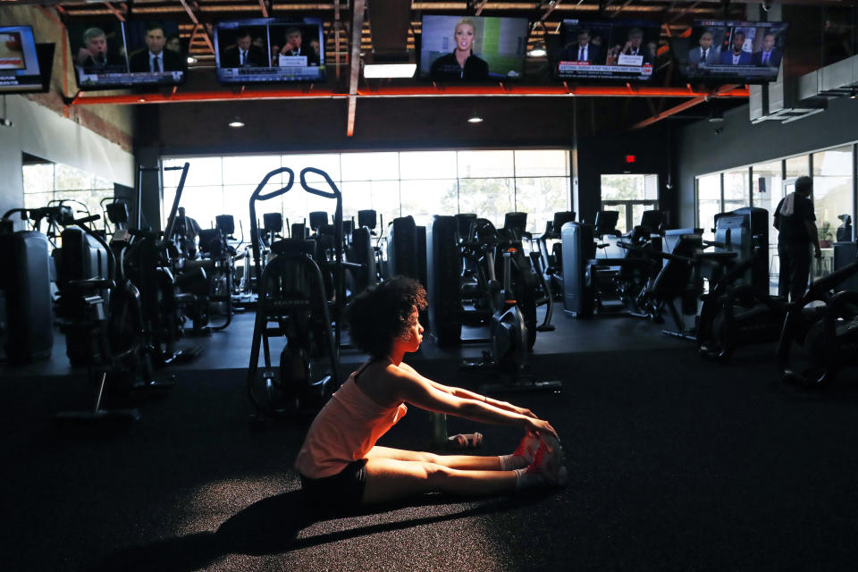 Cindy Alvarez of Jackson, Miss., stretches on the workout mat at Fondren Fitness, while various television screens show different networks views of the Trump impeachment hearings as well as HGTV and ESPN programming, Wednesday, Nov. 13, 2019. (AP Photo/Rogelio V. Solis)