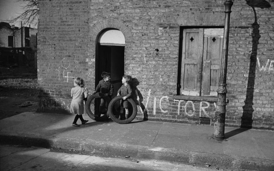 Children playing games in the street in the East End of London, framed by a graffiti slogan for Victory - Charles Hewitt