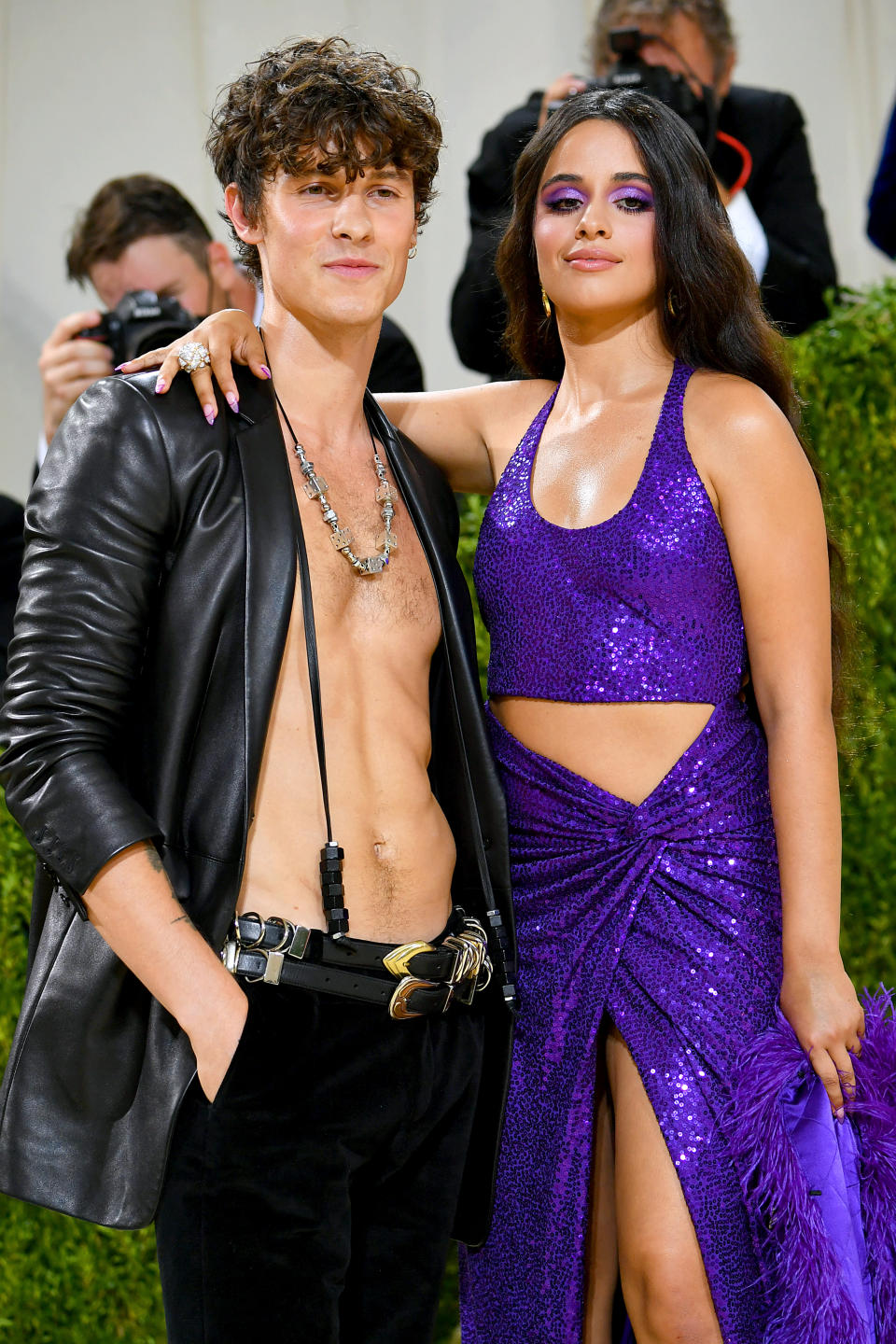 Man in leather jacket and necklaces; woman in purple sequined dress with slit. Both posing on event carpet