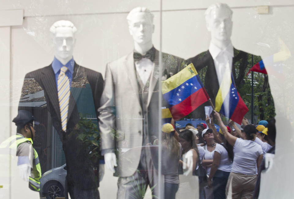 Anti-government demonstrators holding representations of Venezuela's national flag are reflected in a storefront window during a protest in front of an office of the Organization of American States, OAS, in Caracas, Venezuela, Friday, March 21, 2014. Opposition lawmaker Maria Corina Machado is scheduled to speak before the OAS council in a closed-door session Friday in Washington D.C., presenting the situation in her country where at least 28 people have been killed in daily anti-government protests that began in early February. (AP Photo/Esteban Felix)