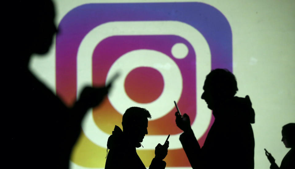 Silhouettes of mobile users are seen next to a screen projection of Instagram logo in this picture illustration taken March 28, 2018.  REUTERS/Dado Ruvic/Illustration