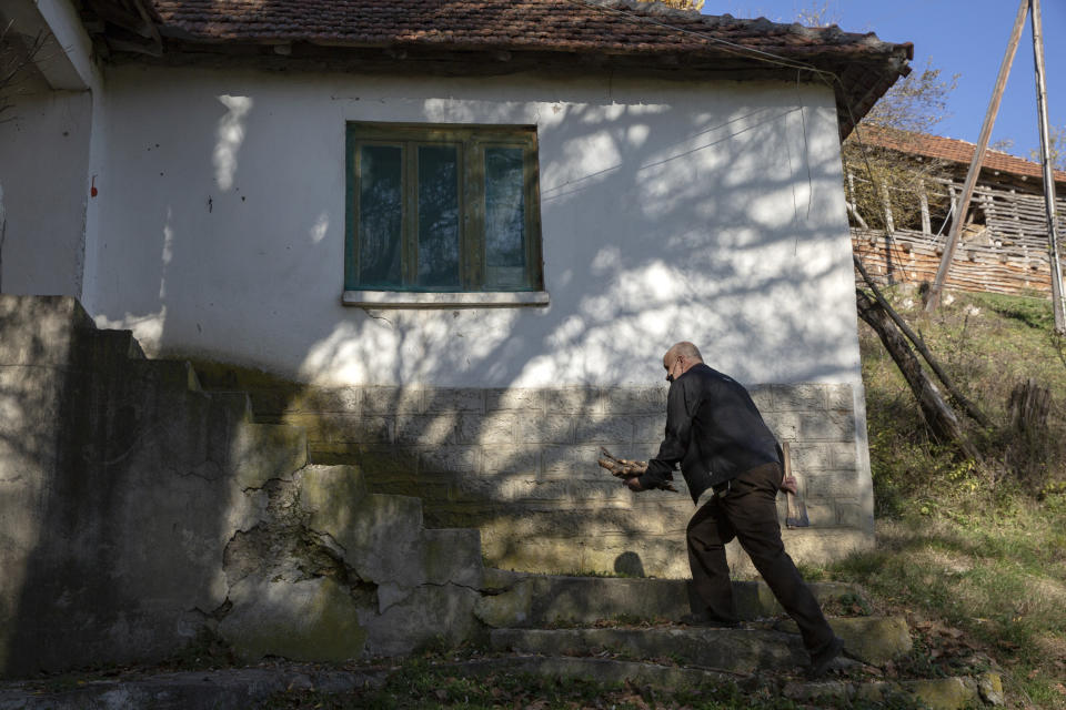 Kosovo Albanian Fadil Rama carries fire wood for a Kosovo Serb Blagica Dicic a lonely 92-year old woman in a remote village of Vaganesh, Kosovo on Thursday, Nov. 19, 2020, abandoned by all her former ethnic Serb neighbors. (AP Photo/Visar Kryeziu)