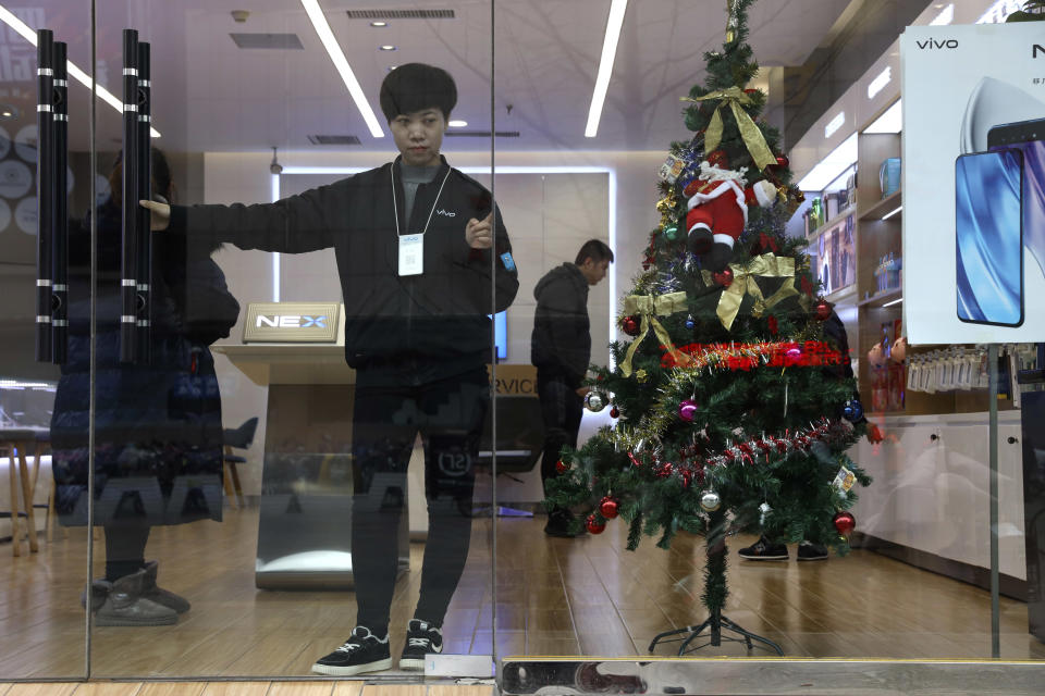 In this Saturday, Dec. 22, 2018, photo, a sales person waits for customers near a Christmas tree decoration in Zhangjiakou in northern China's Hebei province. At least four Chinese cities and one county have ordered restrictions on Christmas celebrations this year. Churches in another city have been warned to keep minors away from Christmas, and at least ten schools nationwide have curtailed Christmas on campus, The Associated Press has found. (AP Photo/Ng Han Guan)