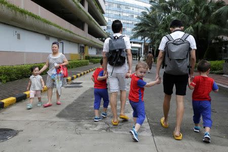 A girl looks at An Hui (L) and his partner Ye Jianbin walking with their sons, An Zhizhong, An Zhiya and An Zhifei at a residential community in Shenzhen, Guangdong province, China September 17, 2018. The triplets were conceived with the help of a German egg donor. REUTERS/Jason Lee