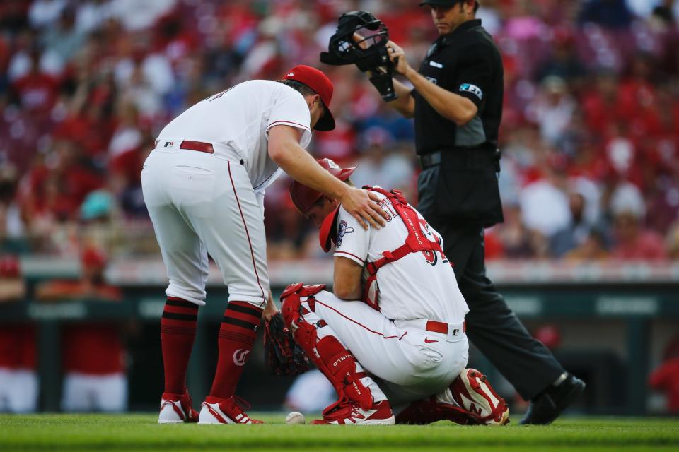Cincinnati Reds catcher Tyler Stephenson crouches in pain next to pitcher Graham Ashcraft, left, after attempting to make a throw to first base in the first inning on Friday, July 22, 2022 at Great American Ball Park.