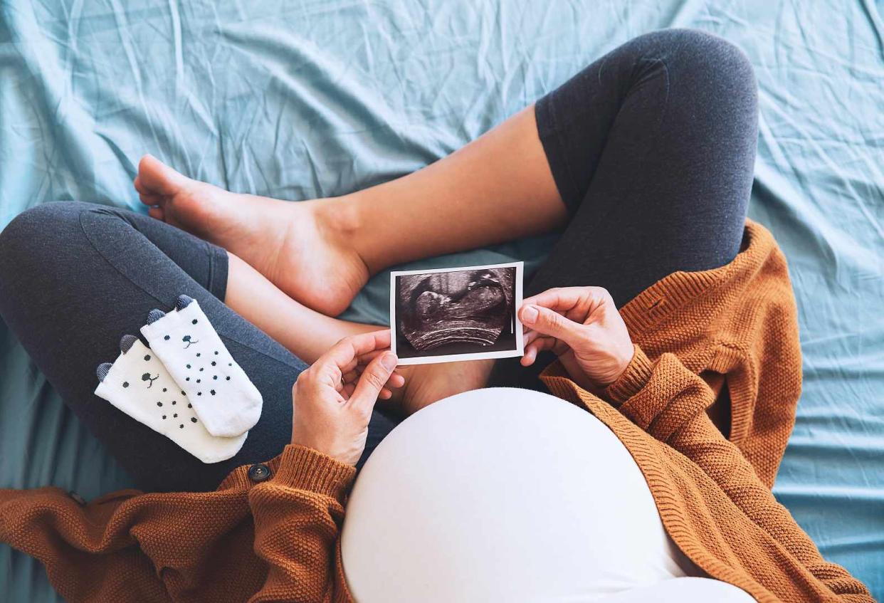 Pregnant Women Sitting on Bed Holding Sonogram and Socks