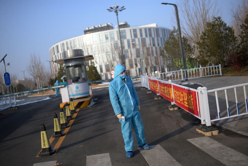 FILE PHOTO: Security guard wearing a protective suit holds a thermometer in front of the entrance to the China Transinfo Technology Co, in the morning after the extended Lunar New Year holiday caused by the novel coronavirus outbreak, in Beijing