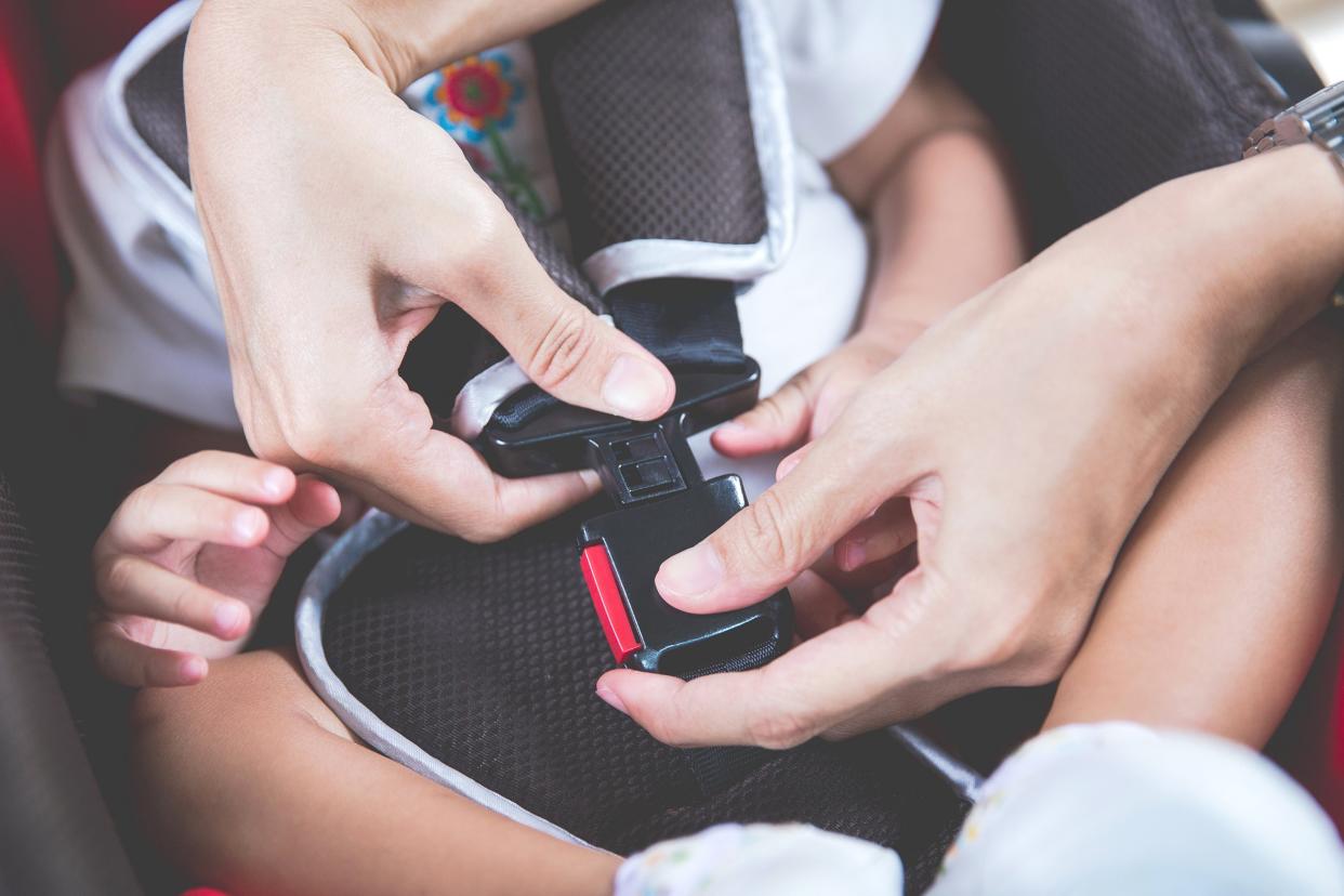 hands of woman is fastening security belt to baby in car seat