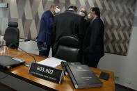 Senators talk behind a desk that has a plaque with the number of COVIVD-19 deaths in Brazil and copies of a Senate commission report on the government's handling of the pandemic, at the Federal Senate in Brasilia, Brazil, Wednesday, Oct. 20, 2021. A senator formally presented the report recommending President Jair Bolsonaro be indicted on criminal charges for allegedly bungling Brazil’s response to the COVID-19 pandemic and pushing the country’s death toll to second-highest in the world. (AP Photo/Eraldo Peres)