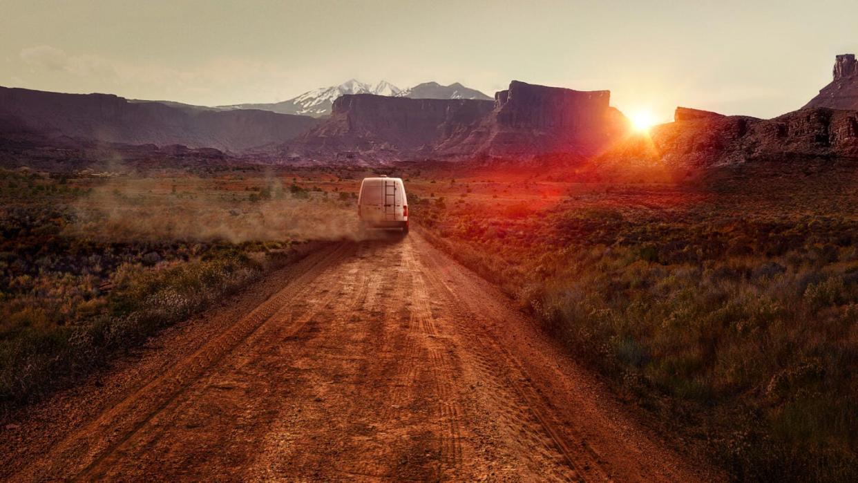 A canyon vista with an RV driving away on a dirt road in the evening light.