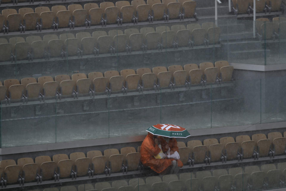 Two spectators take cover during a downpour at center court after the quarterfinal match of the French Open tennis tournament between Japan's Kei Nishikori and Spain's Rafael Nadal was interrupted at the Roland Garros stadium in Paris, Tuesday, June 4, 2019. (AP Photo/Pavel Golovkin)