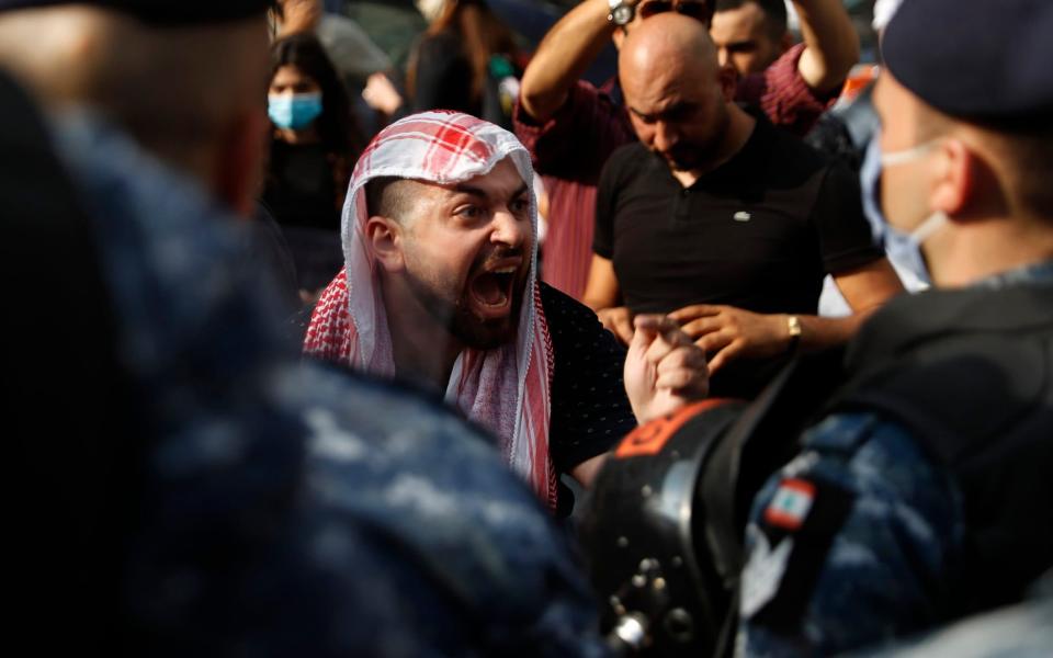 An anti-government protester shouts at riot police, near the scene where a Lebanese man who killed himself on Beirut's commercial Hamra Street -  Hussein Malla/AP