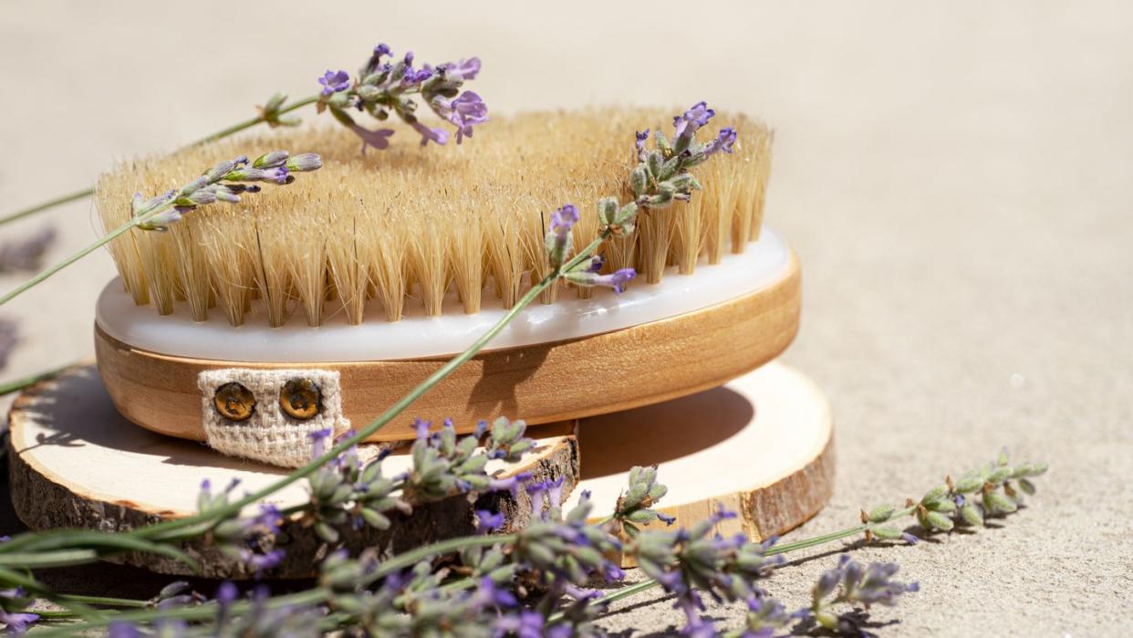 lavender flowers and anti cellulite dry massage brush on concrete beige background