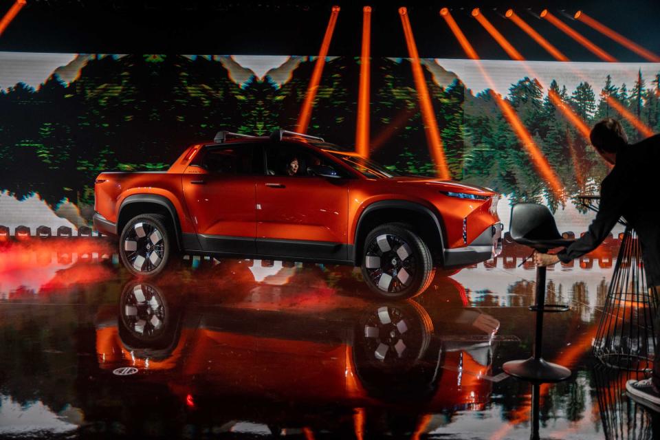 The orange Fisker Alaska electric pickup truck, on stage at an event.