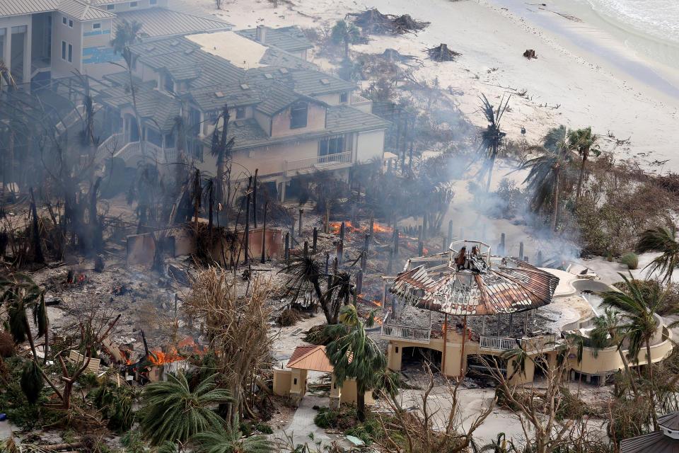 Embers burn in the ruins of homes reduced to ashes, with a roof canopy still standing on one house.