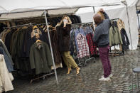 A customer, wearing a face mask to fight against the spread of the coronavirus, tries on a coat at Marolles flea market in Brussels, Tuesday, Oct. 13, 2020. Authorities in Belgium, one of the European countries hit hardest by the coronavirus, are warning that the number of cases is rising at a "quite alarming" rate and that 10.000 people could be catching the virus each day by the end of the week. (AP Photo/Francisco Seco)
