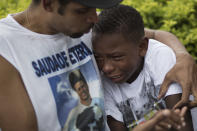 A boy is comforted by a friend wearing a shirt with a photo of Douglas Rafael da Silva Pereira, during Pareira's burial in Rio de Janeiro, Brazil, Thursday, April 24, 2014. A protest followed the burial of Douglas Pereira, whose shooting death sparked clashes Tuesday night between police and residents of the Pavao-Pavaozinho slum. (AP Photo/Felipe Dana)