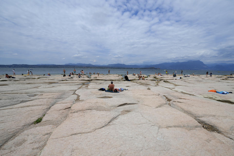 Decenas de personas tomando sol en una parte reseca del Lago Garda de Italia el 12 de agosto del 2022. (AP Photo/Antonio Calanni)