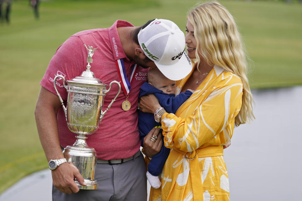 Jon Rahm, of Spain, holds the champions trophy for photographers as he stands with his wife, Kelley Rahm and kisses their child, Kepa Rahm, 11 months, after the final round of the U.S. Open Golf Championship, Sunday, June 20, 2021, at Torrey Pines Golf Course in San Diego. (AP Photo/Marcio Jose Sanchez)