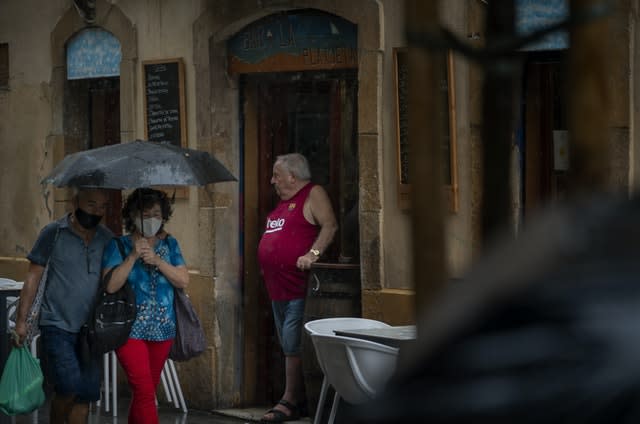 A man stands in a bar entrance as people walk by in Barcelona, Spain