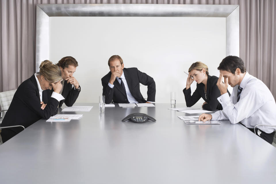 People in business suits sitting around a conference table looking uncomfortable.