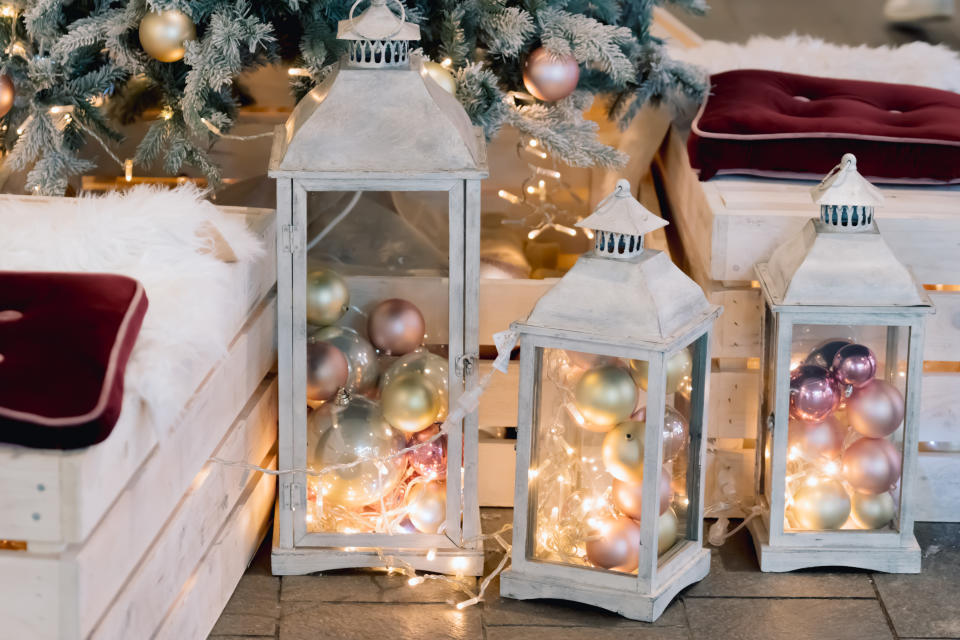 Lantern with holiday baubles on decorated christmas tree background in living room interior. Winter time and lamp on wooden sofa near christmas tree. Cozy vintage holiday home interior