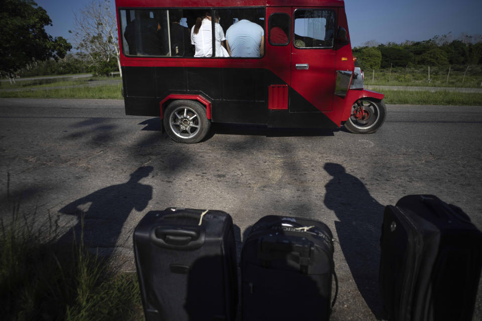 A commuter vehicle is full of people on a highway where the shadows of people with luggage are cast as they wait for an available taxi or bus near Catalina de Guines, Cuba, Friday, May 19, 2023. Cuba has been restricting fuel sales amid a gas shortage. (AP Photo/Ramon Espinosa)