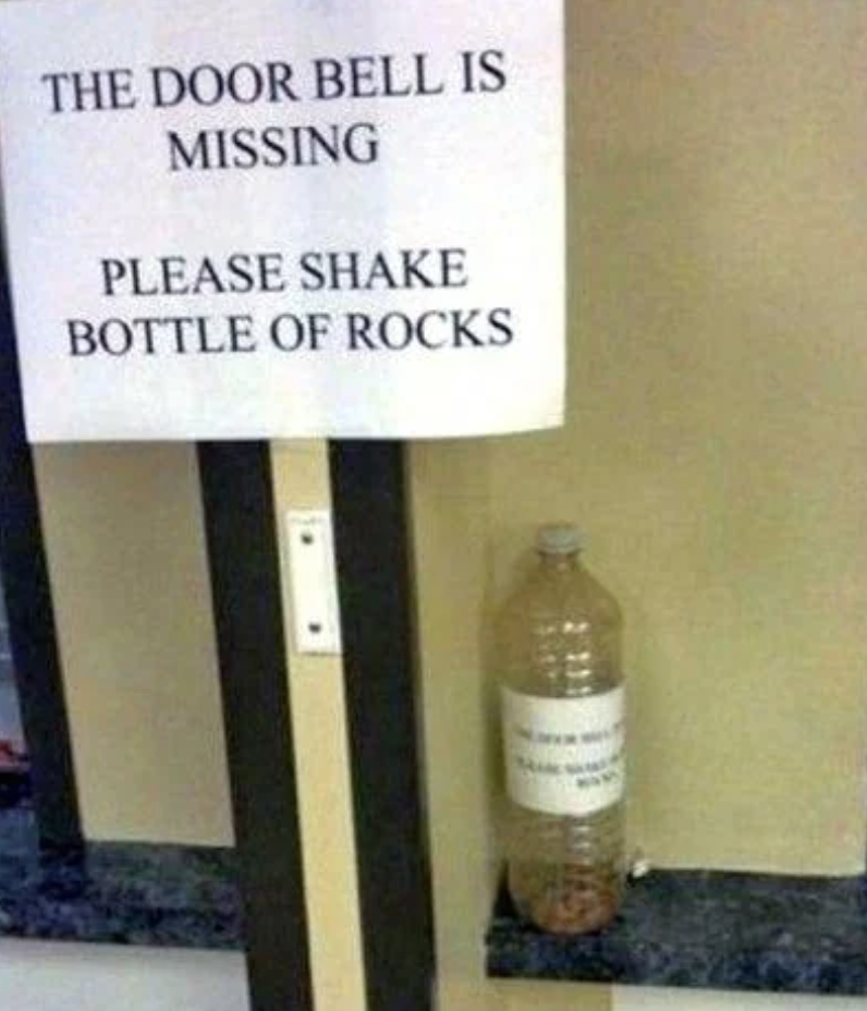 Sign reads "THE DOOR BELL IS MISSING PLEASE SHAKE BOTTLE OF ROCKS" next to a bottle filled with small stones