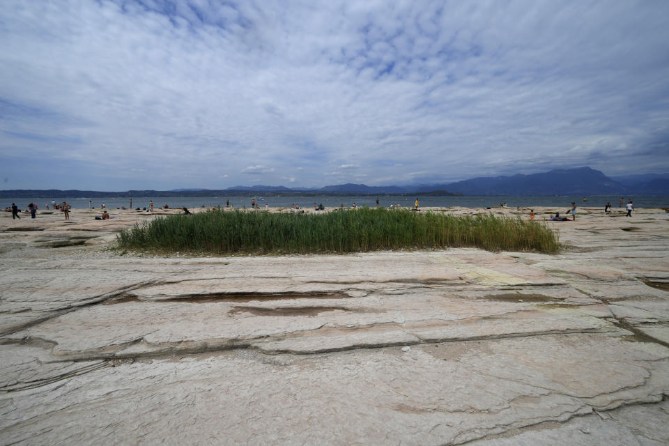 People sunbath on the peninsula of Sirmione, on Garda lake, Italy, Friday, Aug. 12, 2022. Lake Garda water level has dropped critically following severe drought resulting in rocks to emerge around the Sirmione Peninsula. (AP Photo/Antonio Calanni)