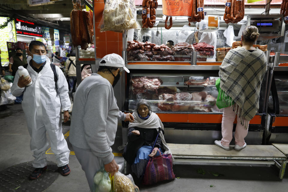 En elderly woman with her mask pulled down begs for change beside a worker offering antibacterial hand gel to passing shoppers and workers to curb the spread of the new coronavirus, inside the Central de Abastos, the capital's main market, in Mexico City, Tuesday, Dec. 8, 2020.(AP Photo/Rebecca Blackwell)