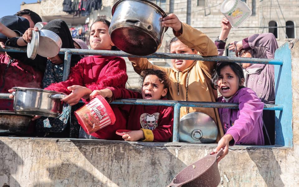 Palestinians gather with pots to receive food at a donation point provided by a charitable organization in Rafah in the southern Gaza Strip