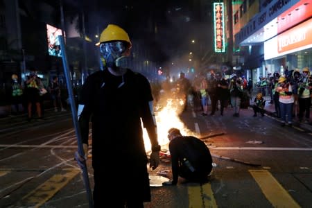 An anti-government protester stands behind a burning barrier during a demonstration, in Hong Kong