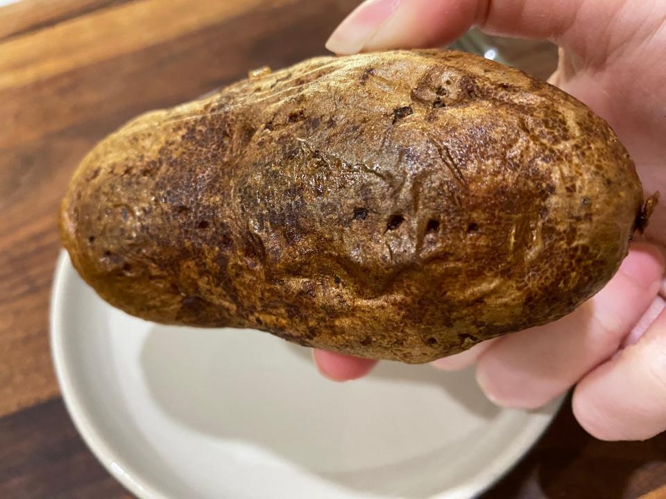hand holding up a baked potato over a white plate