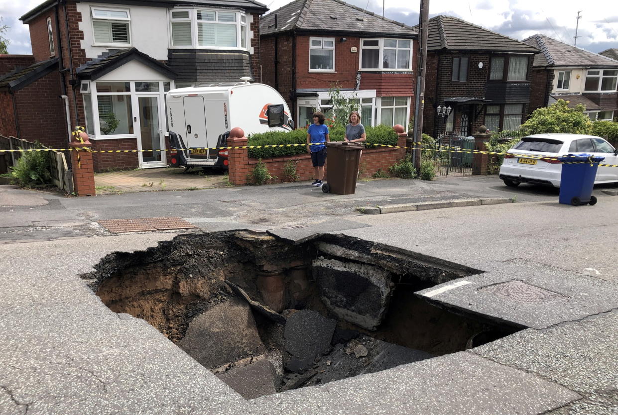 A huge sinkhole has suddenly appeared in the middle of a busy road - leaving homeowners fuming.  See SWNS story SWLShole.  The ground gave way to the massive chamber, measuring roughly six feet deep and ten feet wide, today (Mon) on Heywood Road, Prestwich, Grtr. Manchester.  Traffic was brought to a standstill following the shocking incident, with a hasty perimeter set up around it by police and locals.  But locals who gathered at the chasm vented their anger at the poor quality of the road running past their properties, where most are valued at around £300,000. 