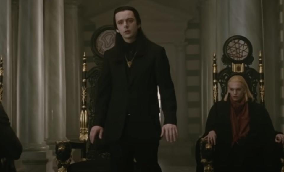 Aro wearing a suit over a shirt with a high collar and a necklace