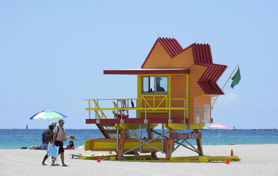 FILE - In this Aug. 11, 2020, file photo, beach goers walk past one of the lifeguard towers designed by architect William Lane during the coronavirus pandemic, on Miami Beach, Florida's famed South Beach. As states around the country require visitors from areas with high rates of coronavirus infections to quarantine upon arrival, children taking end-of-summer vacations to hot spots are facing the possibility of being forced to skip the start of in-person learning at their schools. (AP Photo/Wilfredo Lee)