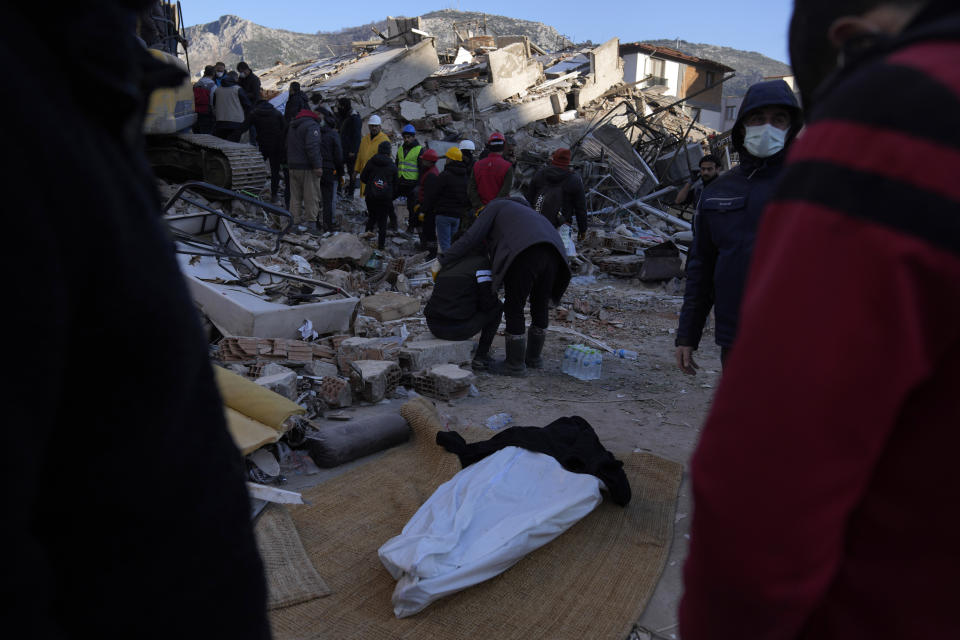 People stand around a dead body was taken out from the rubble of a destroyed building in Antakya, southern Turkey, Thursday, Feb. 9, 2023. Tens of thousands of people who lost their homes in a catastrophic earthquake huddled around campfires in the bitter cold and clamored for food and water Thursday, three days after the temblor hit Turkey and Syria. (AP Photo/Khalil Hamra)