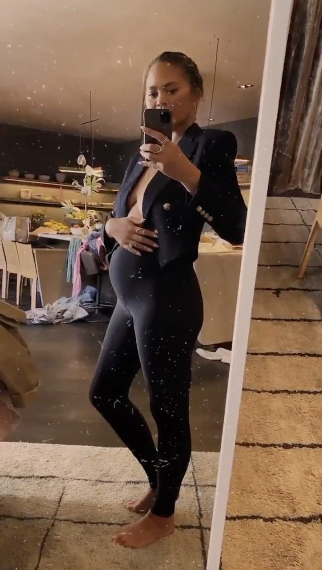 Chrissy Teigen cradles her baby bump in a paid of black leggings