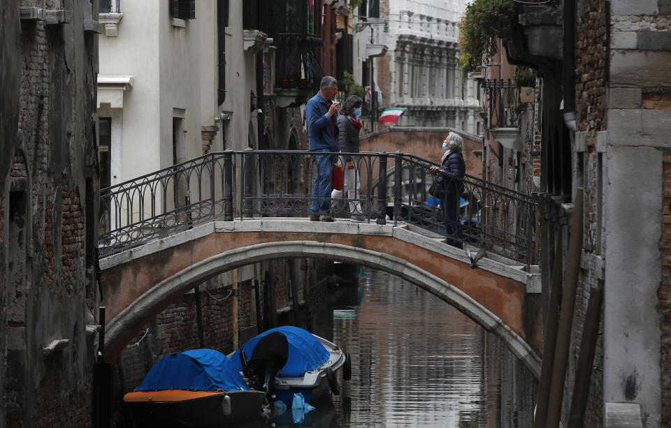 In this picture taken on Wednesday, May 13, 2020, people talk to each other on a bridge in Venice, Italy. Venetians are rethinking their city in the quiet brought by the coronavirus pandemic. For years, the unbridled success of Venice's tourism industry threatened to ruin the things that made it an attractive destination to begin with. Now the pandemic has ground to a halt Italy’s most-visited city, stopped the flow of 3 billion euros in annual tourism-related revenue and devastated the city's economy. (AP Photo/Antonio Calanni)