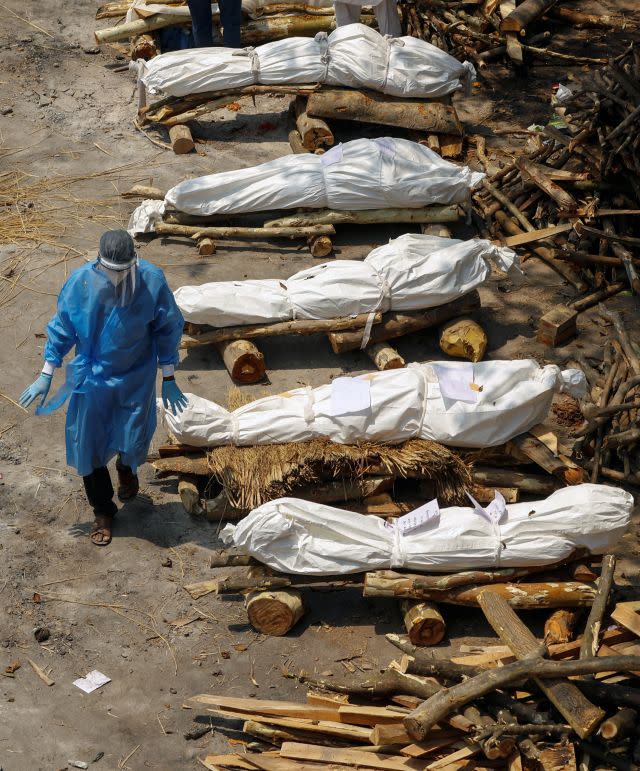 A health worker wearing PPE walks past the funeral pyres of COVID-19 victims during a mass cremation at a crematorium in New Delhi 