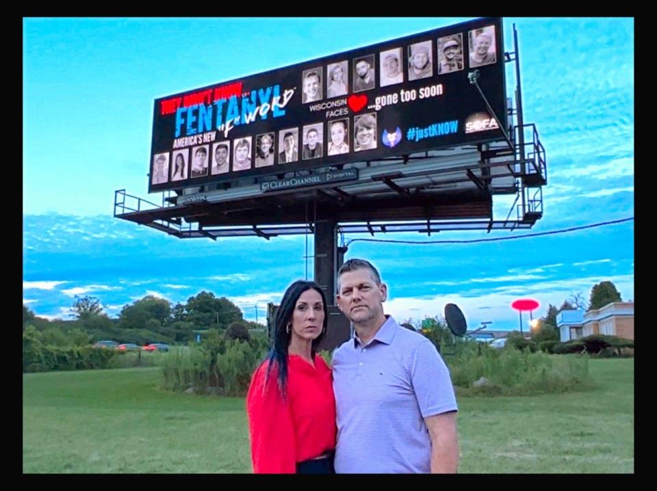 Erin and Rick Rachwal stand in front of a billboard featuring their son and others who died from fentanyl poisoning.