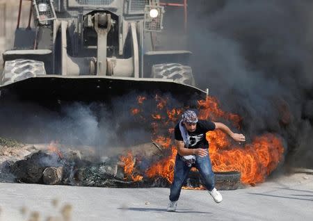 A Palestinian man runs in front of an Israeli military machinery during clashes with Israeli troops in the West Bank village of Khobar near Ramallah July 22, 2017. REUTERS/Mohamad Torokman