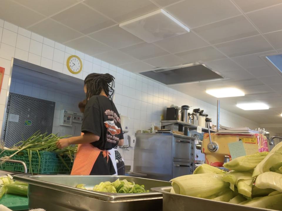 A woman wearing an orange apron in the kitchen handling green onions and leeks.