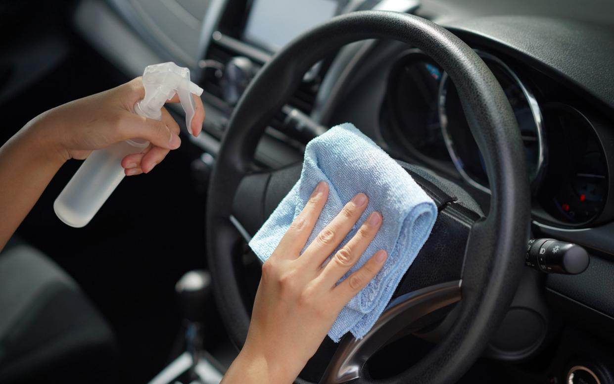 Picture shows woman cleaning car interior with cloth and disinfectant spray