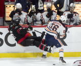 Players on the bench cover up as Edmonton Oilers right wing Kailer Yamamoto sends Ottawa Senators defenseman Mike Reilly into the boards during the first period of an NHL hockey game Wednesday, April 7, 2021, in Ottawa, Ontario. (Adrian Wyld/The Canadian Press via AP)