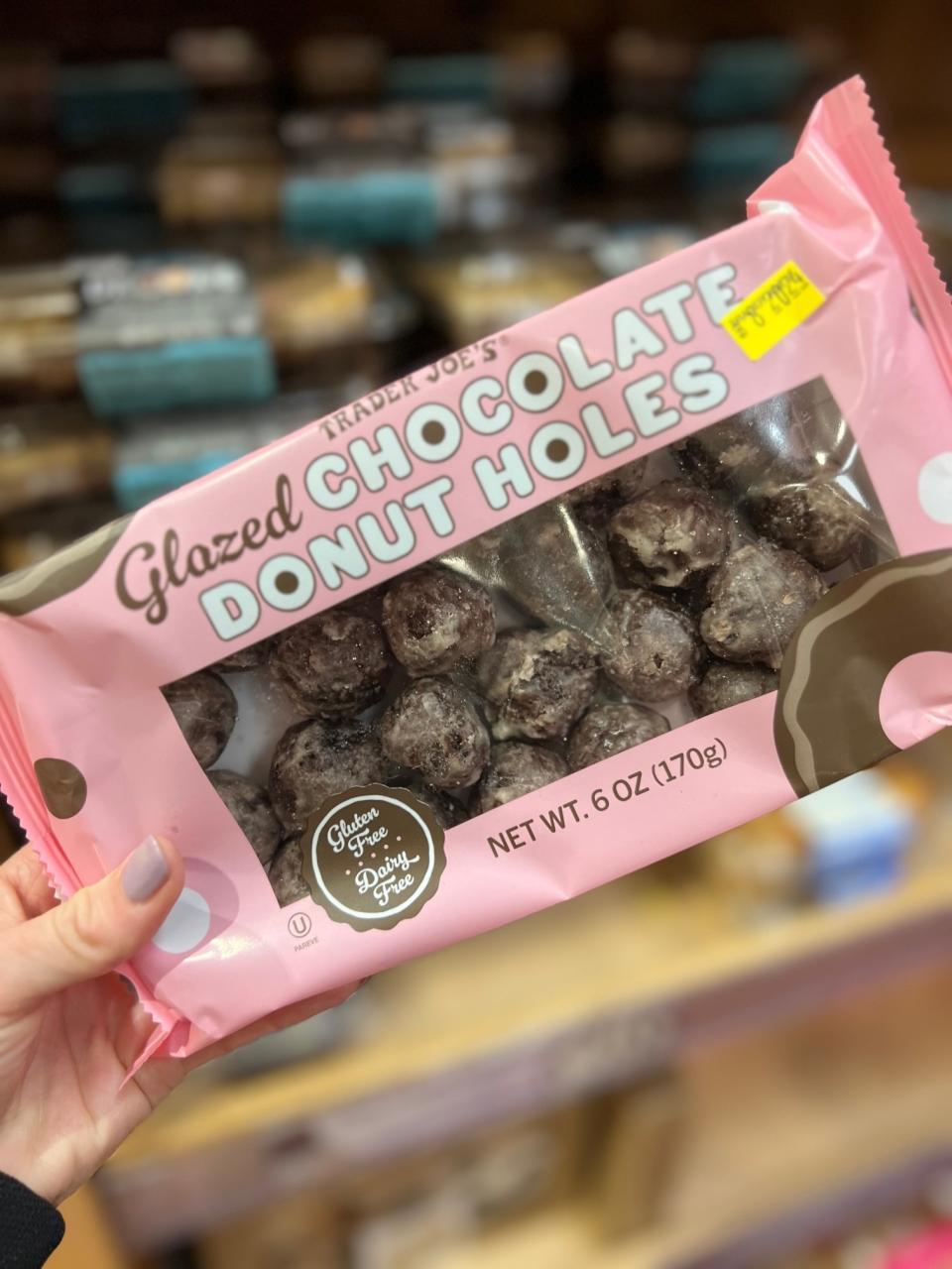 Hand holding a package of Trader Joe's Glazed Chocolate Donut Holes on a store shelf